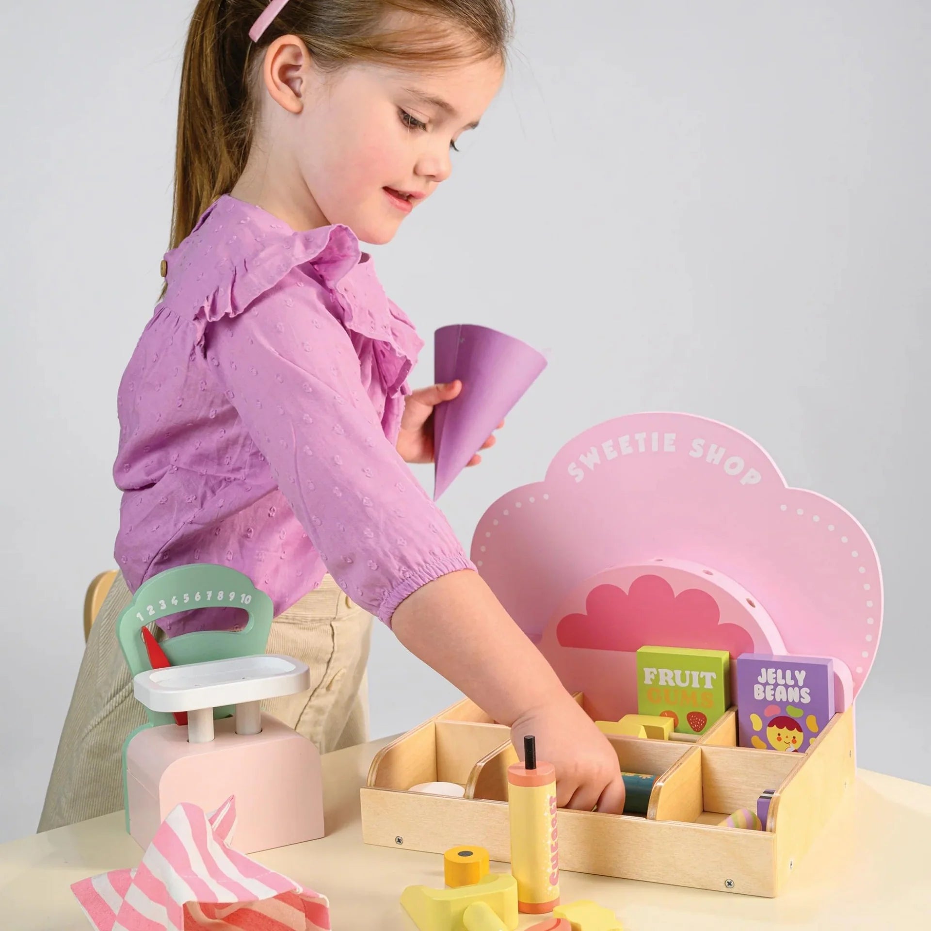 Child playing with a toy sweet shop set on a table.